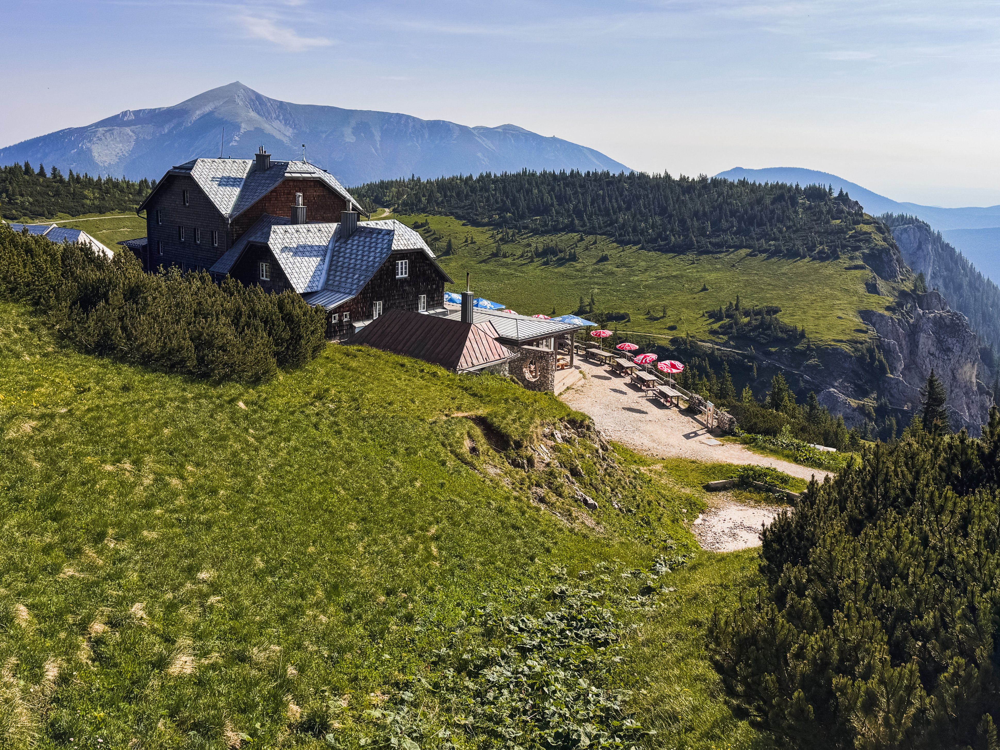 Mountain landscape with the Ottohaus on the Rax, surrounded by green meadows and a mountain in the background.