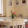 Dining area in a vacation home with round table, bouquet of flowers in a vase and decorative pictures on the wall.