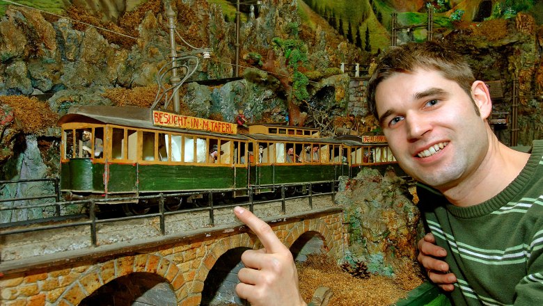 A man points to a model railroad in an alpine landscape.
