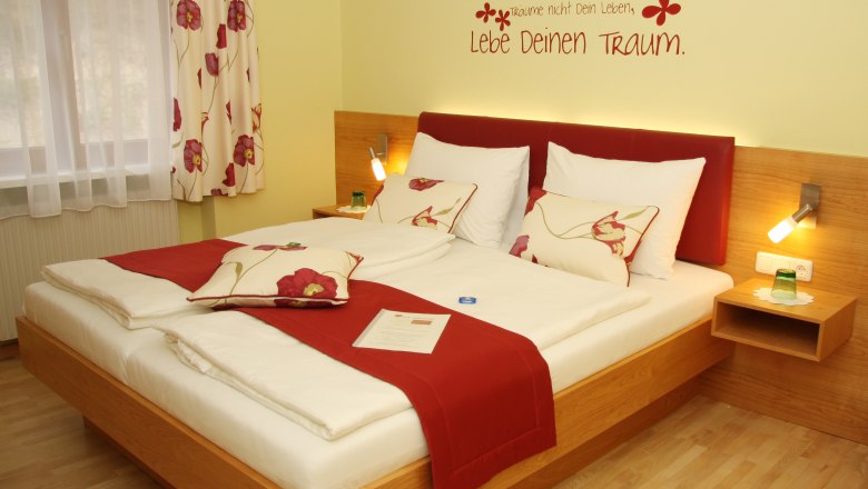 A cozy hotel room with a double bed, red accents and an inspiring wall quote.
