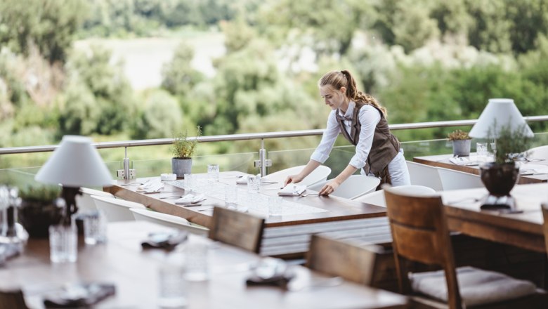 A waitress sets tables on a terrace with a view of the Donau-Auen National Park.
