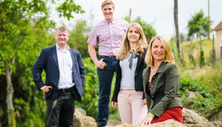 Four people pose outside on a rock, surrounded by trees and plants.