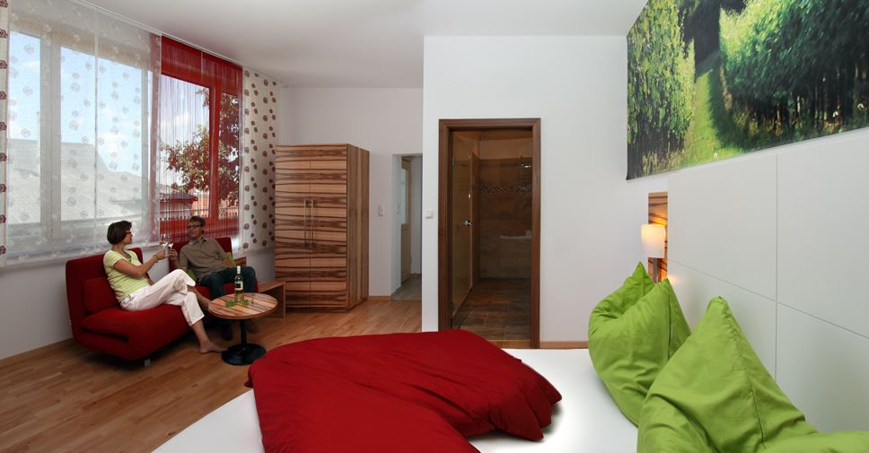 Modern guest room with red sofa, green-red bed and large window.