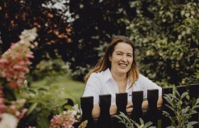 Woman in white shirt smiling behind a wooden fence in the garden.