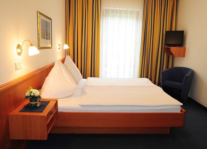 A hotel room with a double bed, blue curtains and a small TV on the wall.