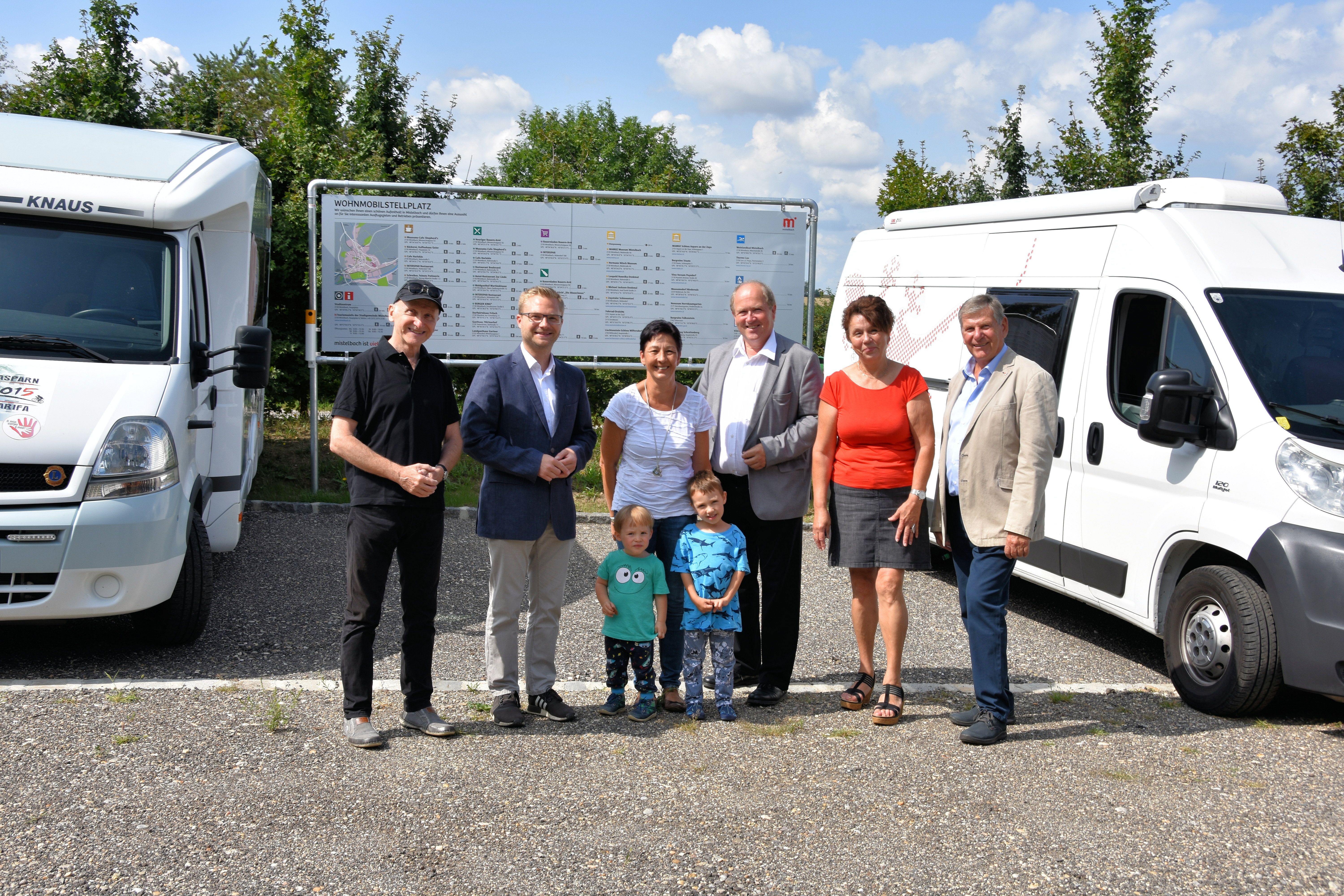 Group of people in front of mobile homes and a sign on a pitch.