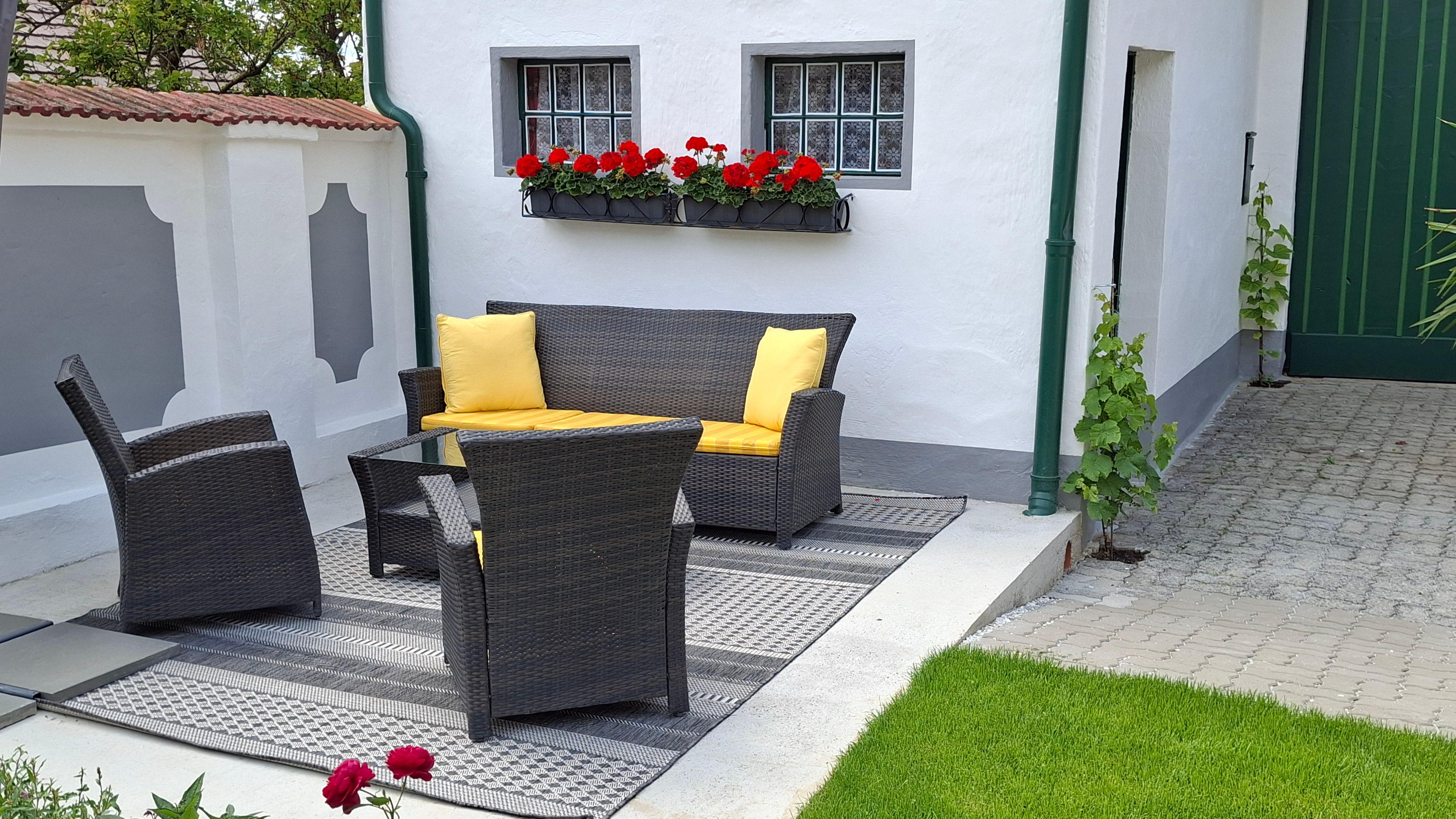 Terrace with rattan furniture and yellow cushions, surrounded by white walls and red flowers.