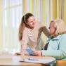 A woman smilingly talks to another woman at a table with documents.