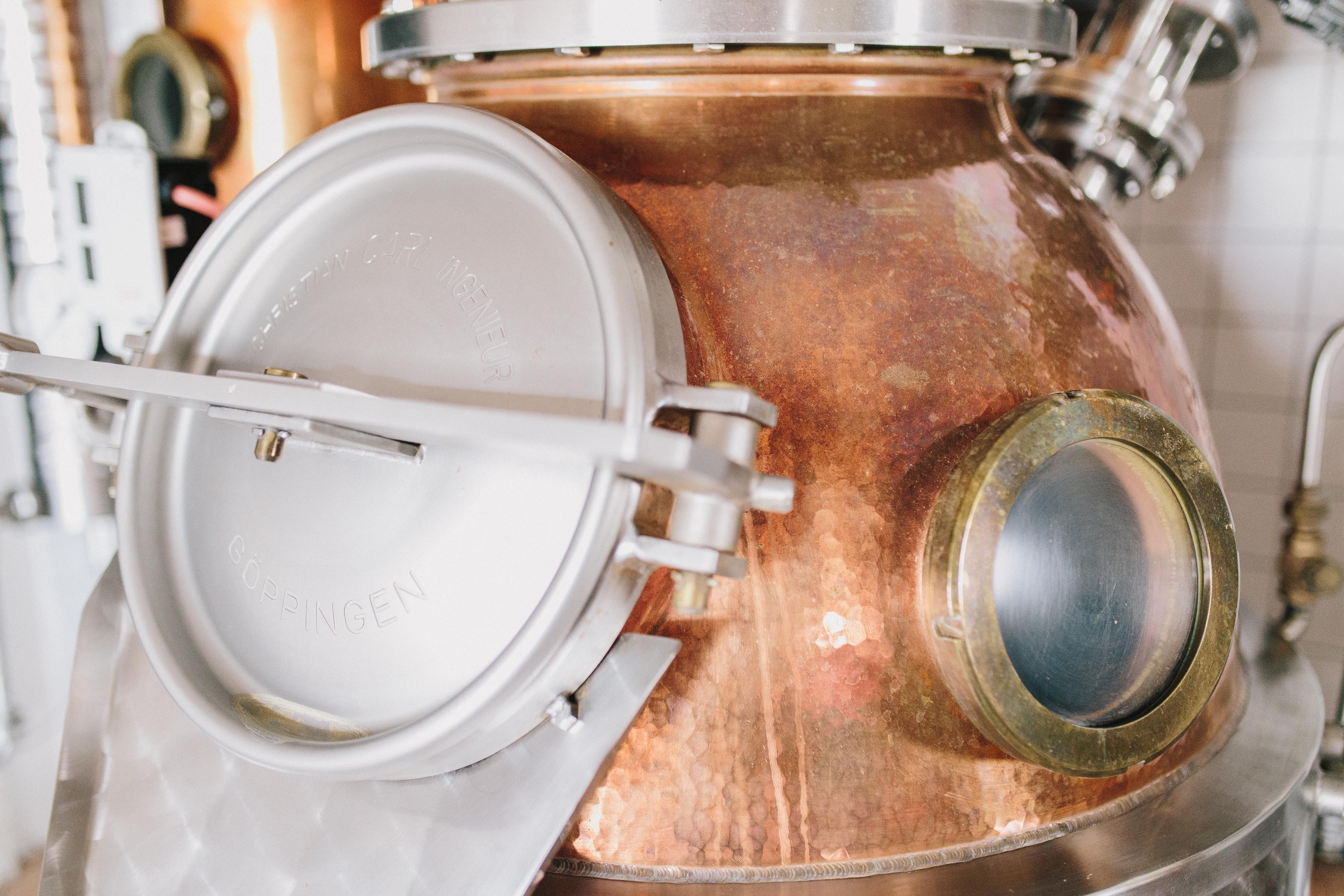 Close-up of a copper still with metal closure and viewing window.