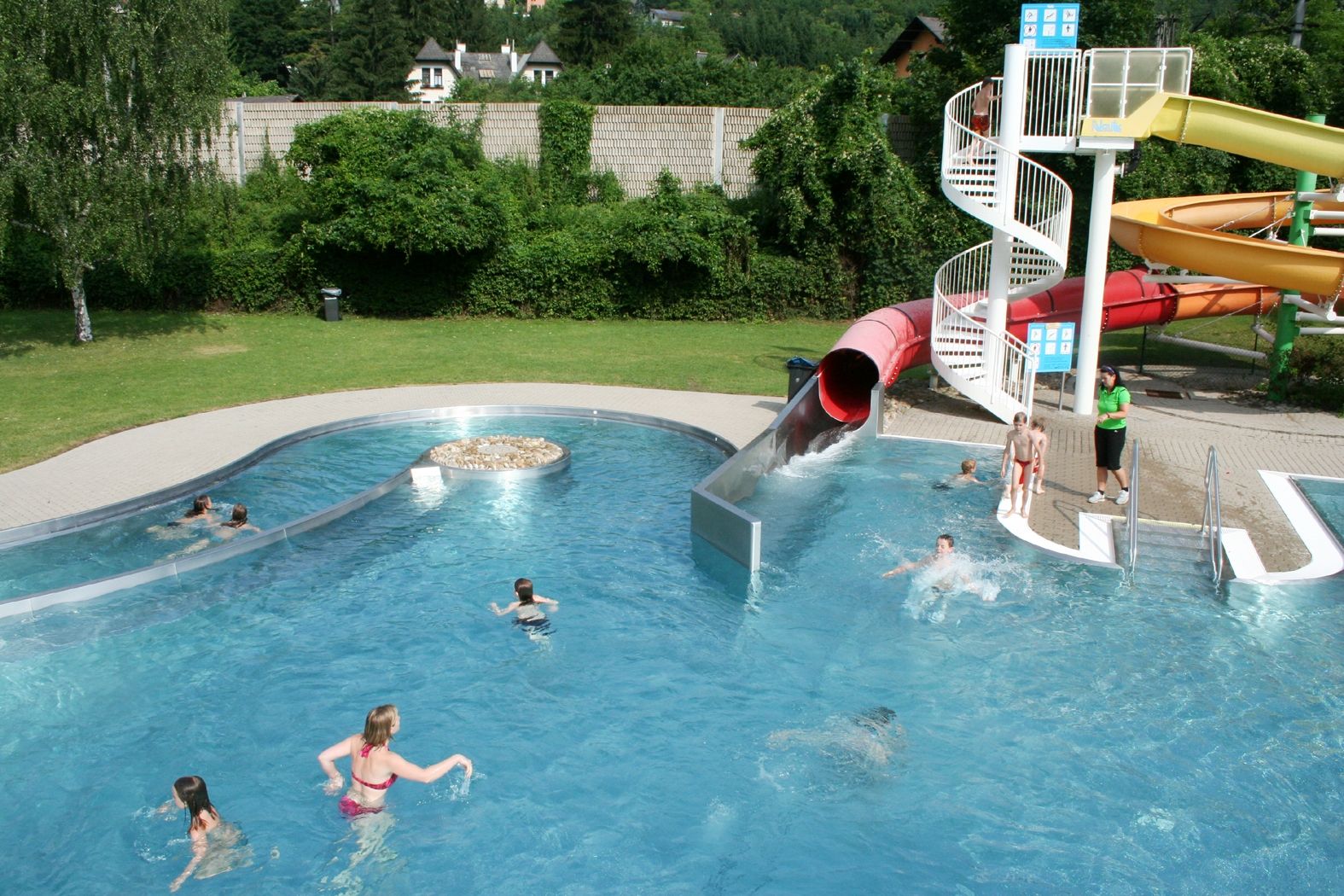 An outdoor pool with a water slide and several people in the water.