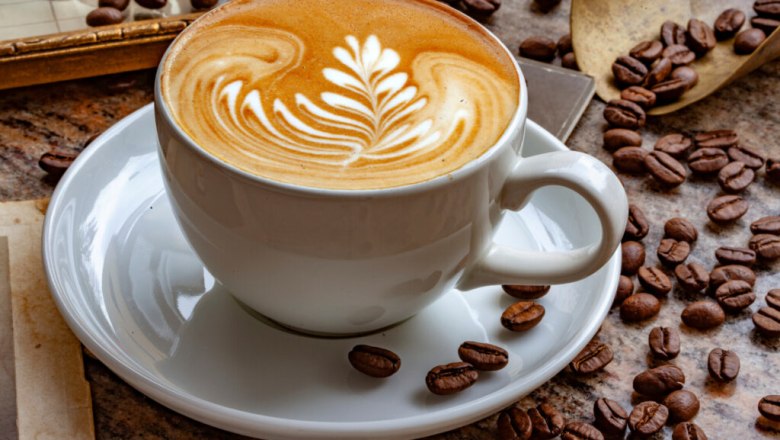 A cup of cappuccino with latte art on a table, surrounded by coffee beans.