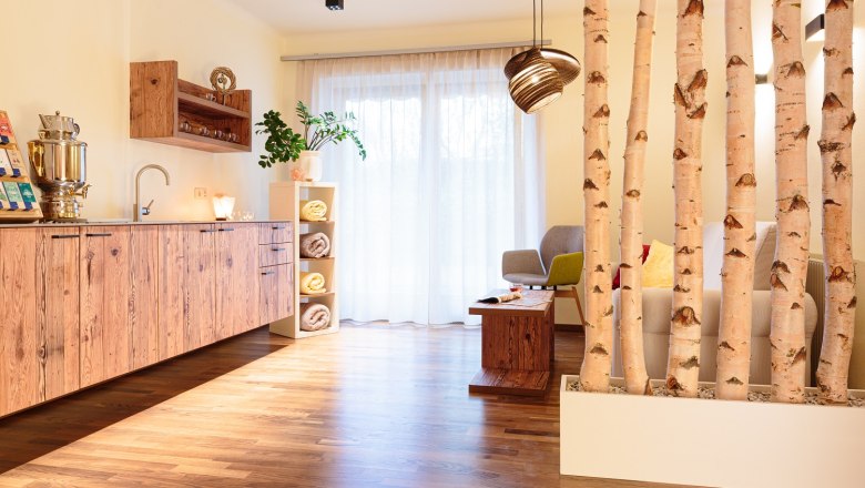 A cozy relaxation room with wooden furniture, plants and birch trunks as room dividers.