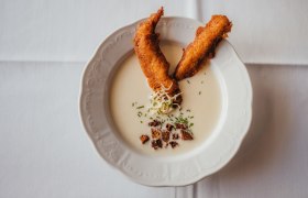 Creamy soup with smoked trout strips and herbs on a white plate.