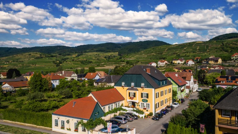 Exterior view, © Donauhof/ Marcel Musiol Rural houses in a green hilly landscape under a blue sky with clouds.