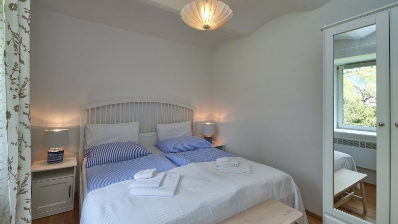 Comfortable bedroom with double bed, blue bed linen, bedside tables and a closet with mirror.
