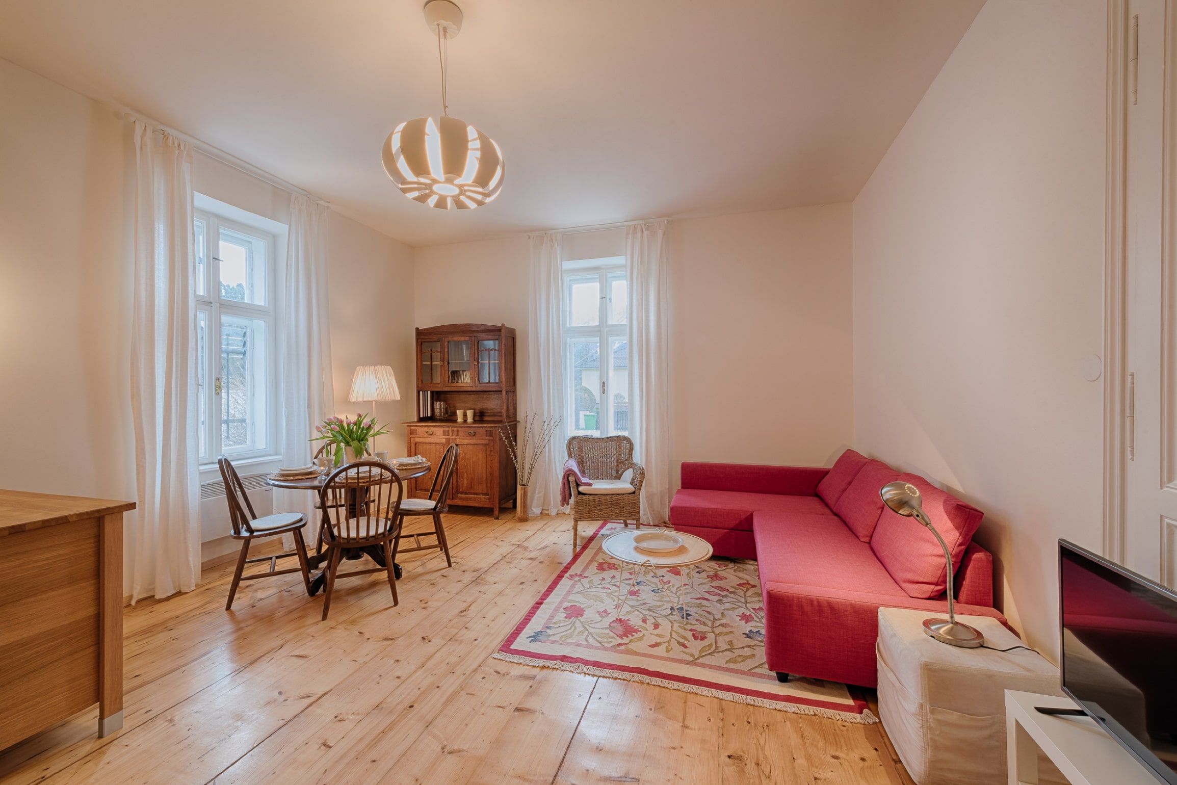 Cozy living room with red sofa, wooden floor and dining table.