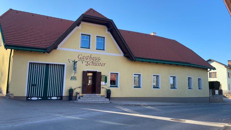 Yellow building with a red roof and the inscription 'Gasthaus Schuster'.