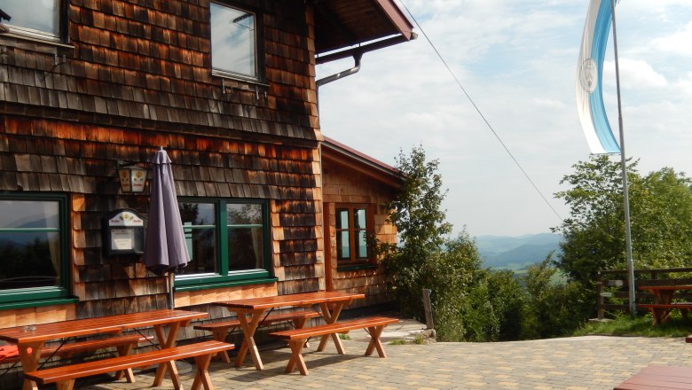 Wooden hut with terrace and benches, flag blowing in the wind.
