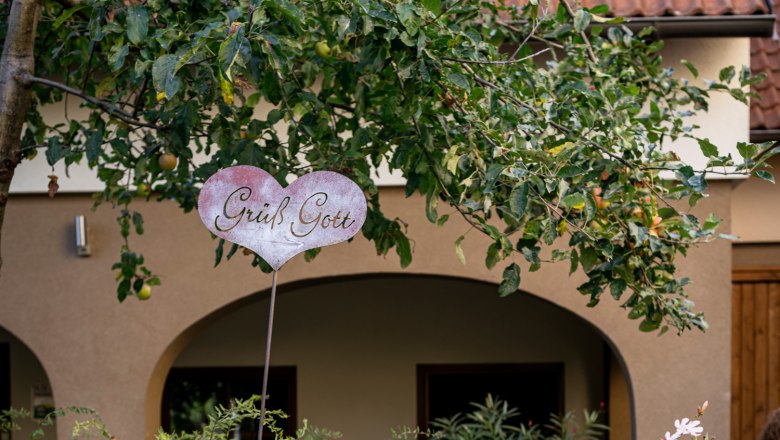 An inner courtyard with plants, a wooden bed and a sign saying 'Gr&uuml;&szlig; Gott'.