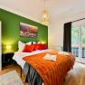 Cozy bedroom with green painted wall, double bed with orange blankets and pillows, lamp and balcony.