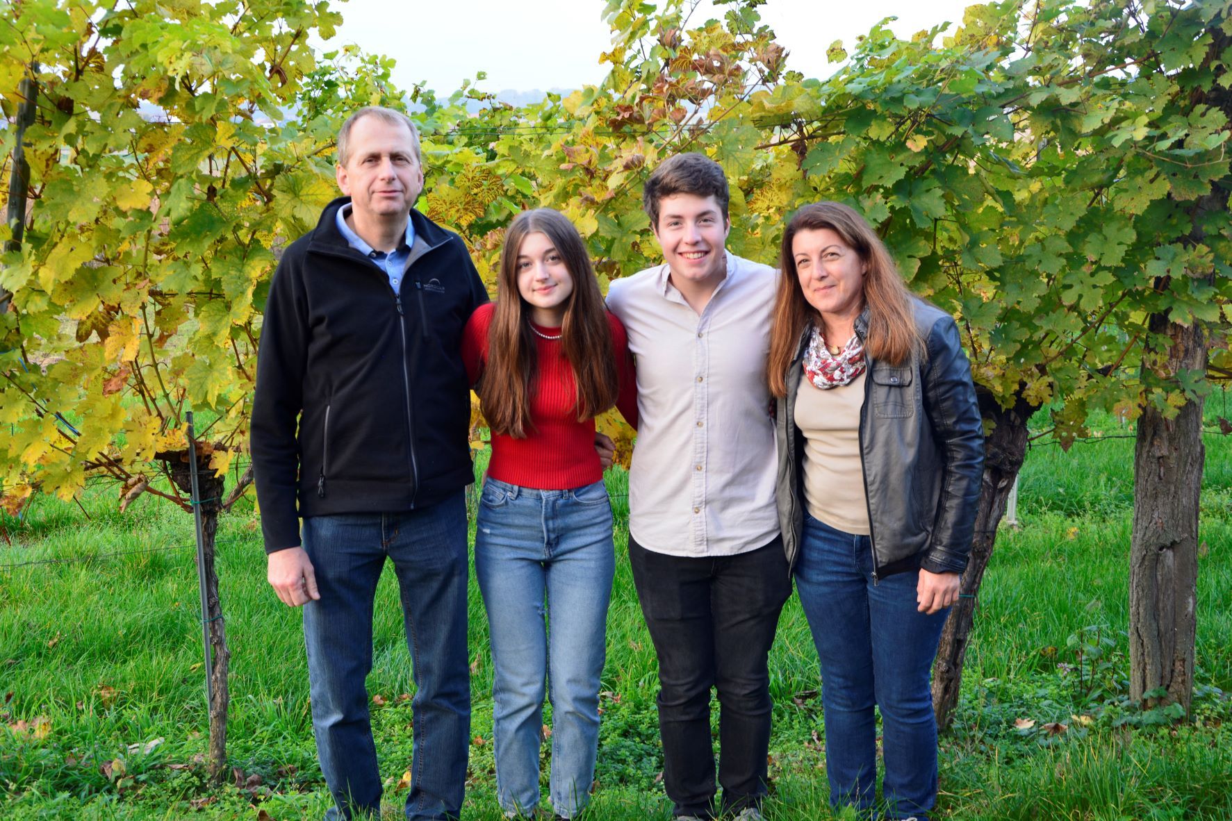 Four people stand smiling in front of vines outside.