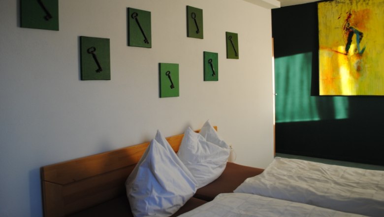 A room with two beds, green pictures of keys on the wall and a yellow painting.