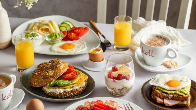 Breakfast table with bread rolls, cold cuts, fried egg, yogurt with berries, orange juice and coffee.