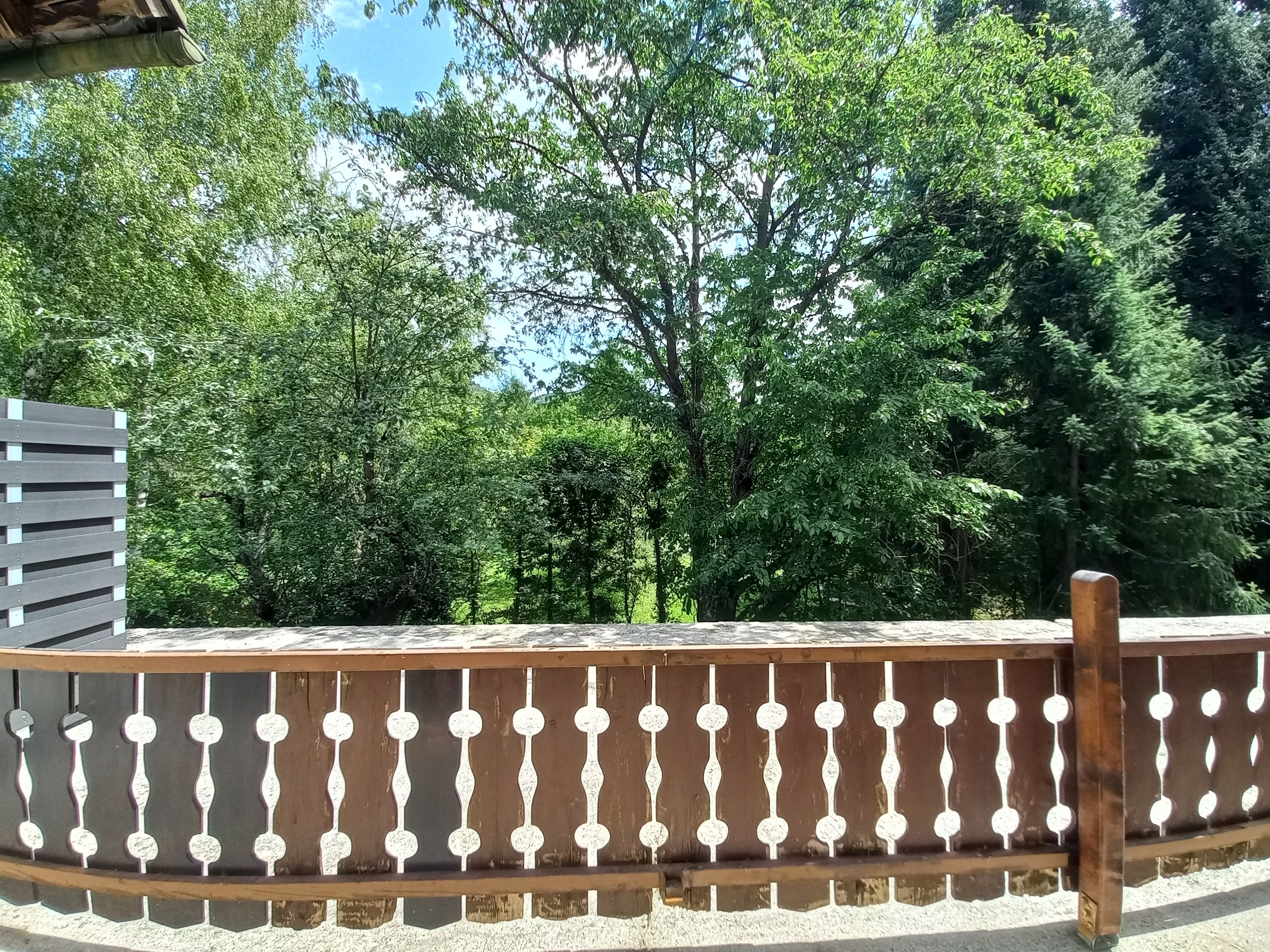 Wooden terrace with decorative railing and view of green trees in the background.