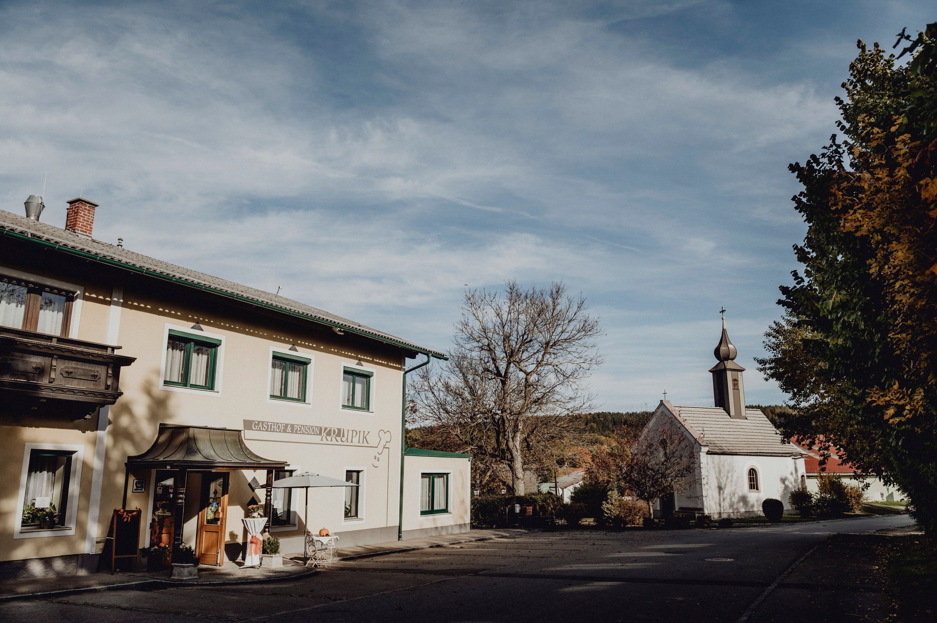 Inn and church in Steinbach near Nagelberg, surrounded by trees and blue sky.
