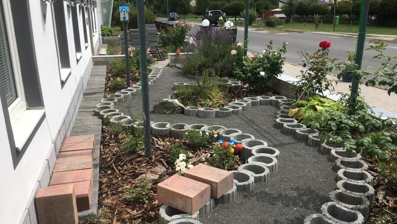 A small garden with roses and a curved path made of concrete blocks next to a building.
