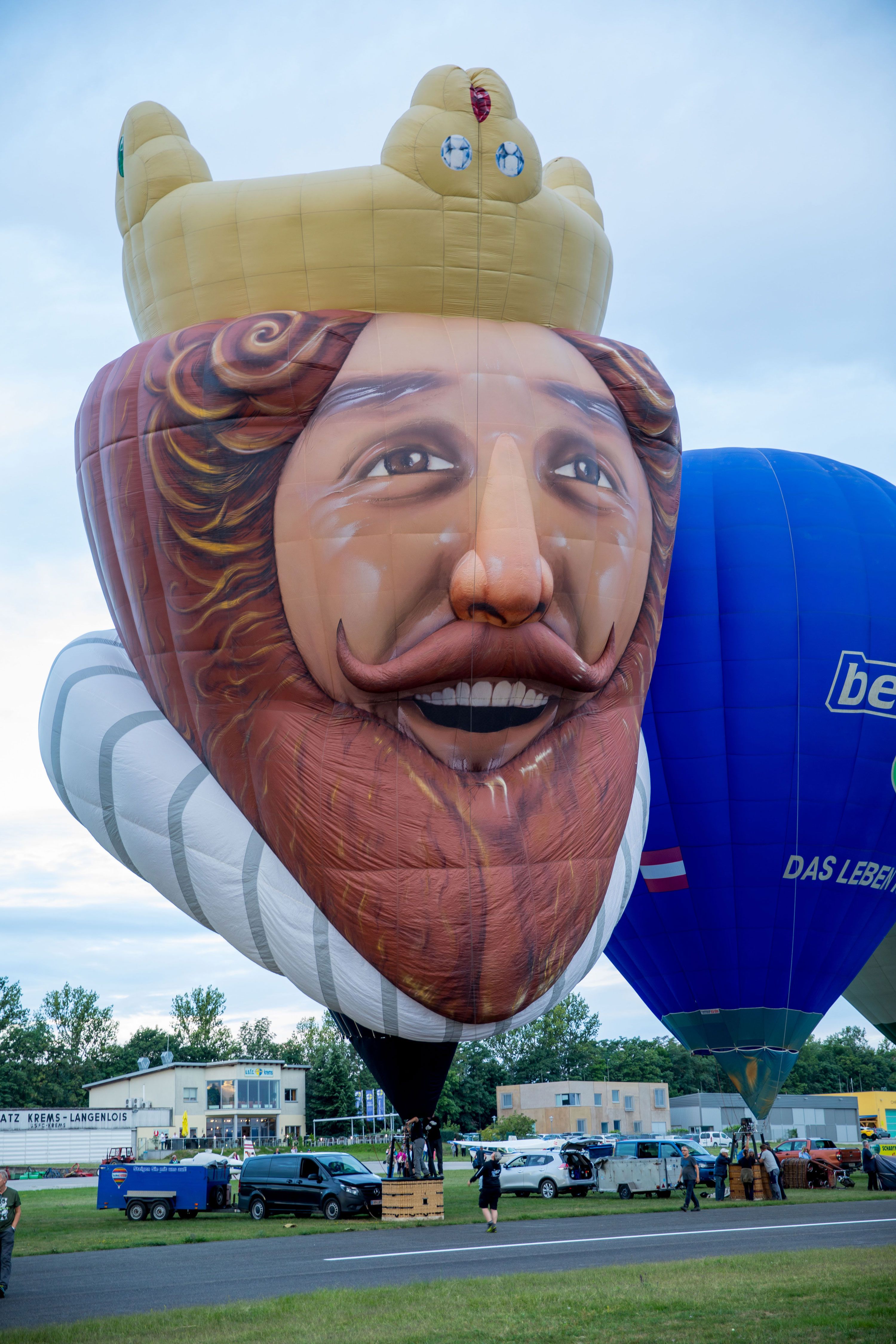 Hot air balloon in the shape of a smiling king with a crown at a balloon festival.