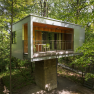 Modern tree house in the forest with balcony and glass front.