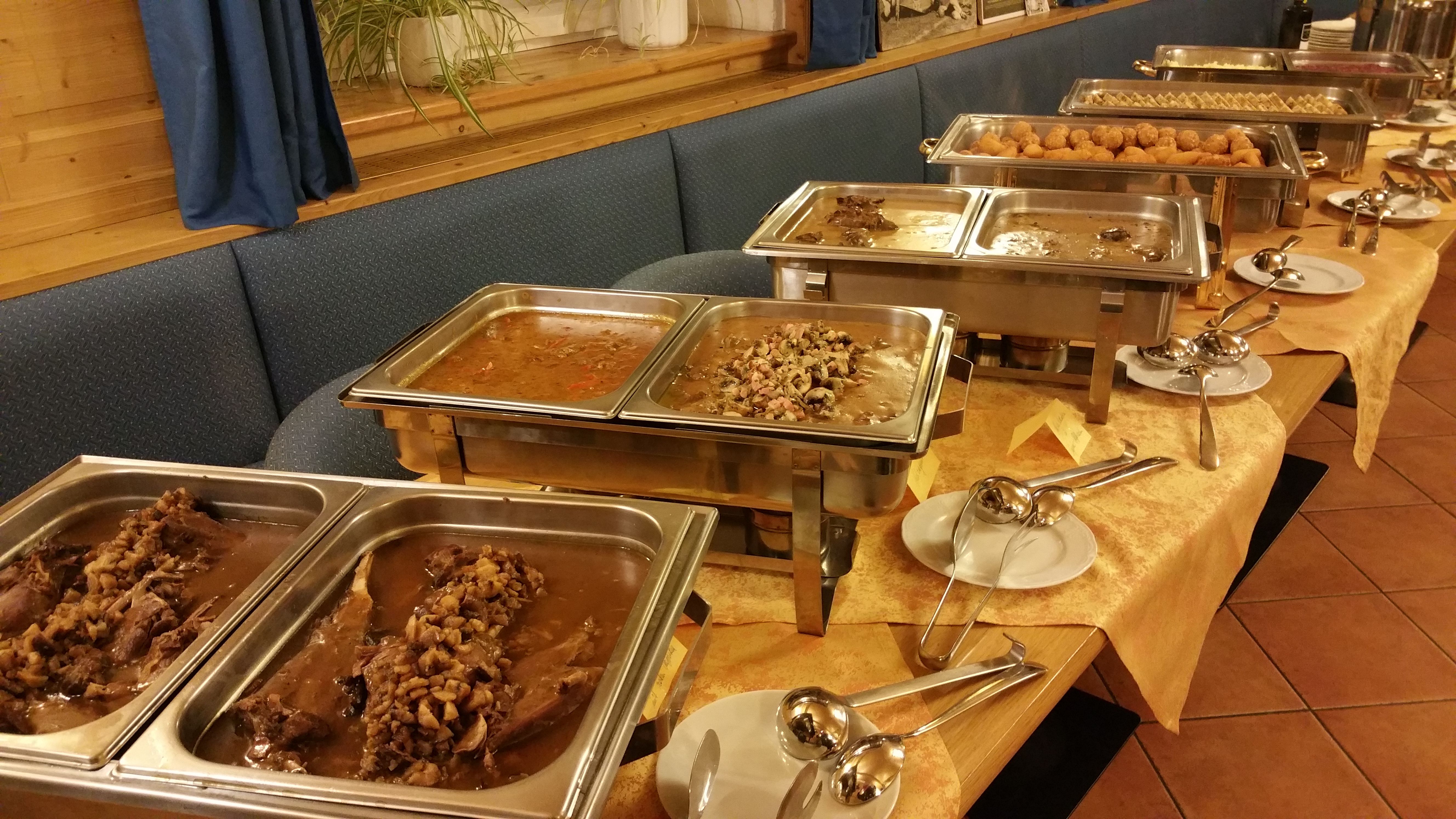 A buffet with various hot dishes in stainless steel containers on a table.