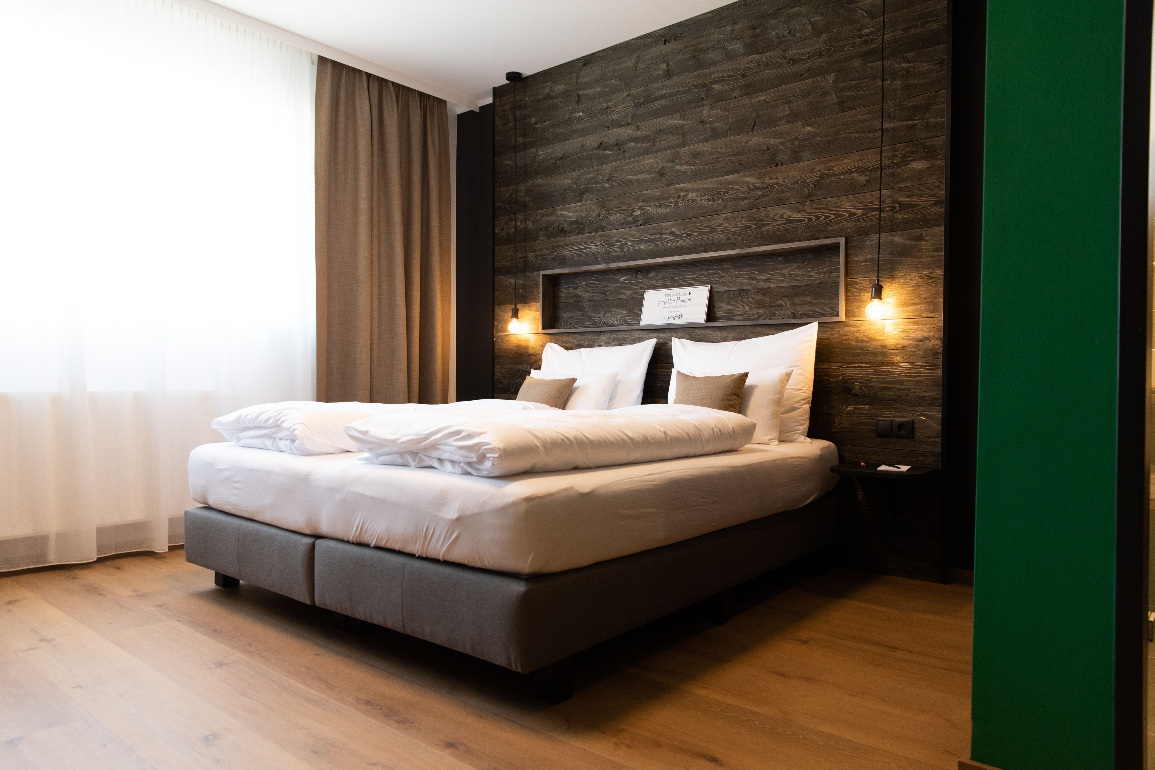 Modern hotel room with large bed, wooden wall and hanging lamps.
