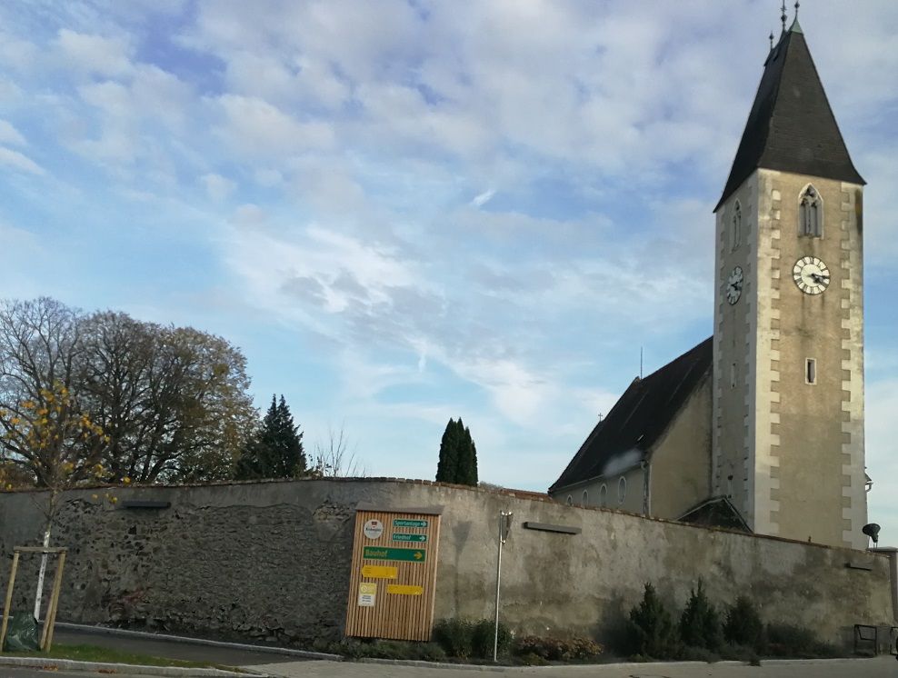 Church with tower and clock in Hafnerbach, surrounded by a wall.
