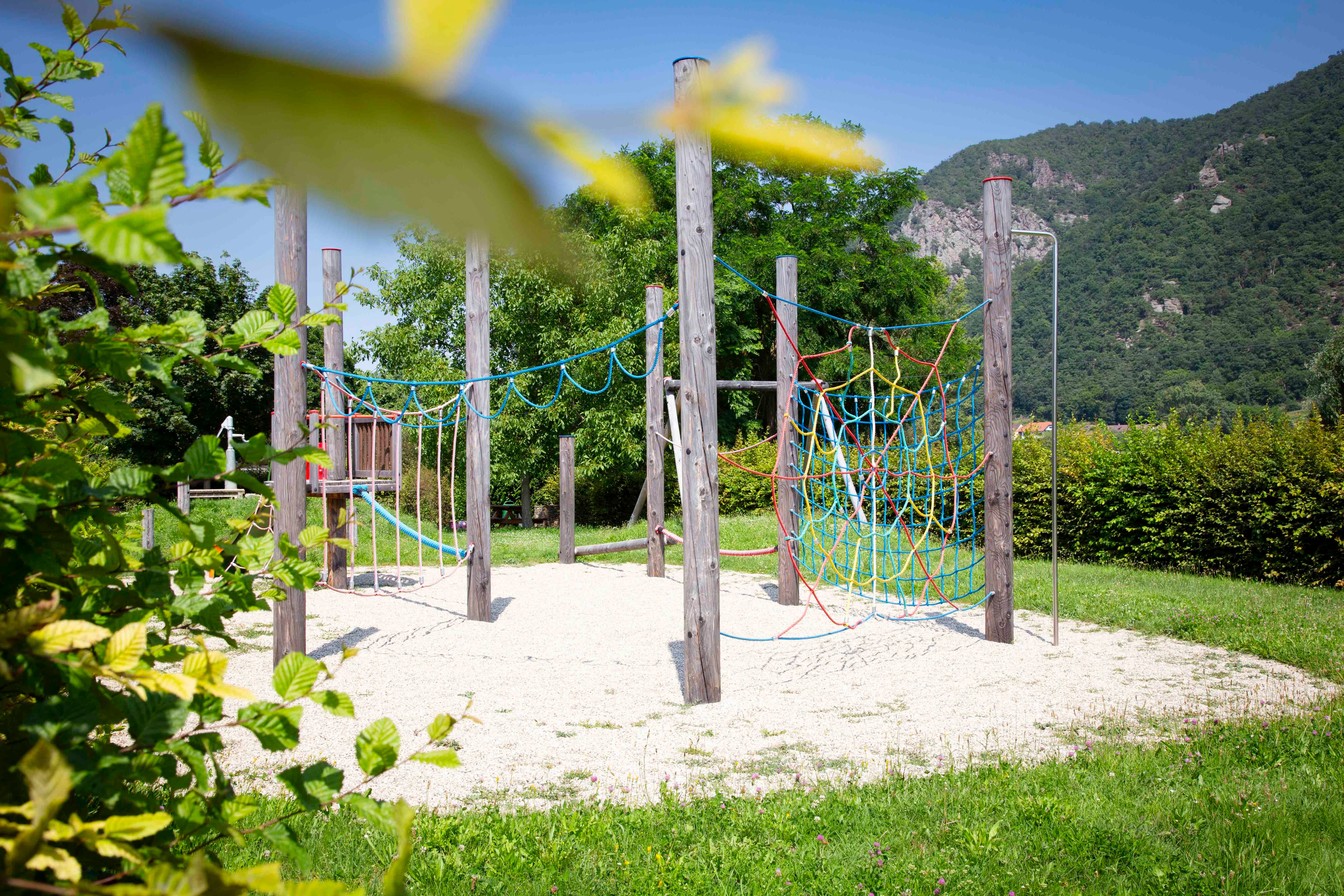 An adventure playground with climbing frames and nets in a green setting with mountains in the background.