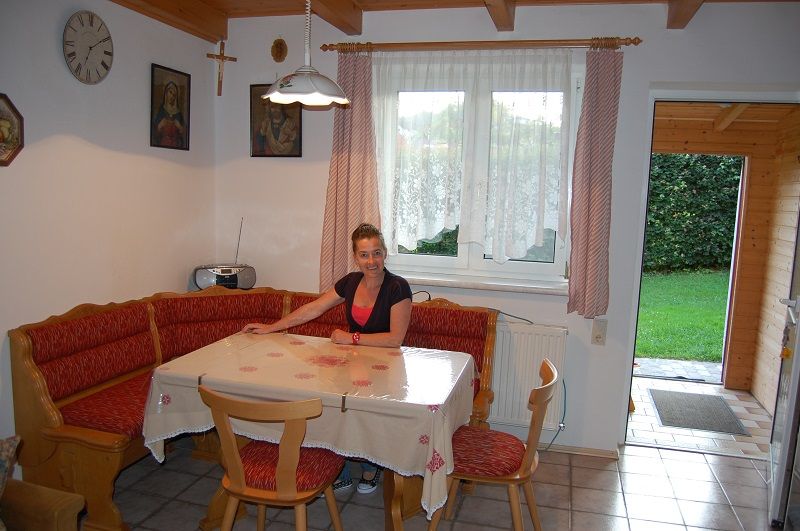 A woman sits at a dining table in a cozy kitchen with a corner bench and red cushions.