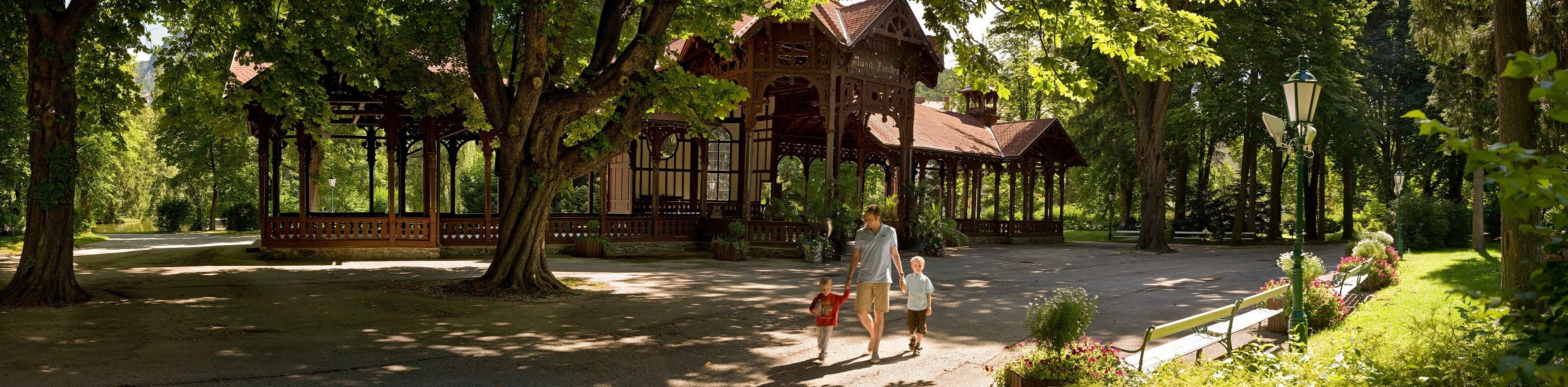 A pavilion in a green park with one adult and two children.
