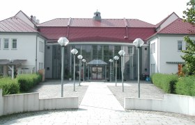 Entrance to a modern cultural center with glass fa&ccedil;ade and red roofs.