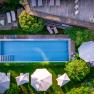 Aerial view of a pool with surrounding sun loungers and parasols in a garden.