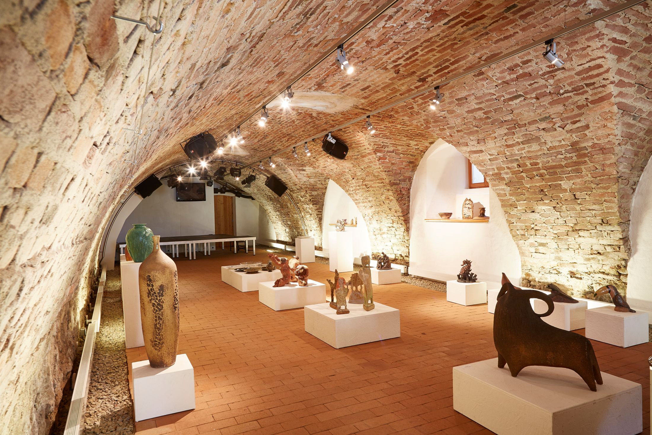 A vaulted cellar with works of art on plinths, illuminated by ceiling spotlights.