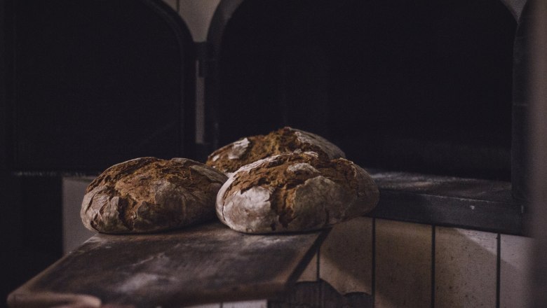Three loaves of bread on a wooden slider in front of an oven.