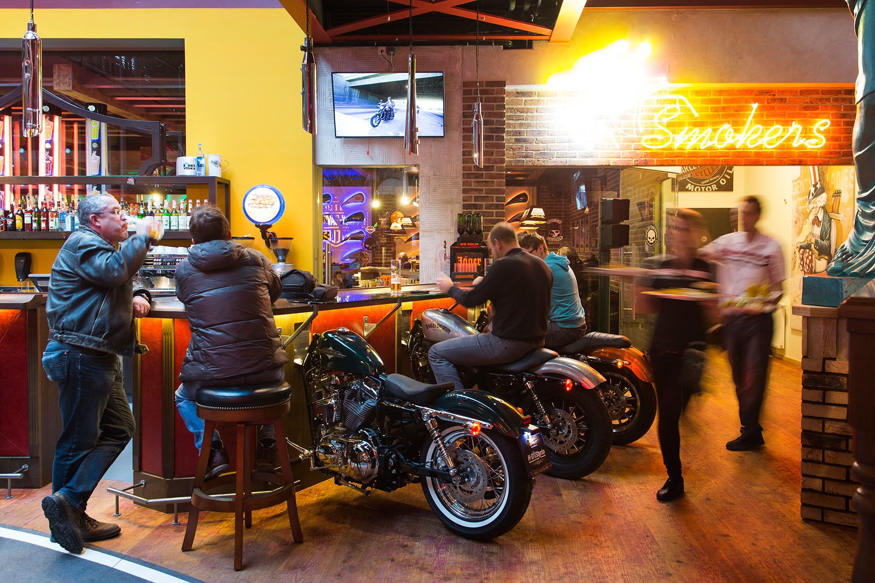 Bar with motorcycles as seating, neon light and guests.