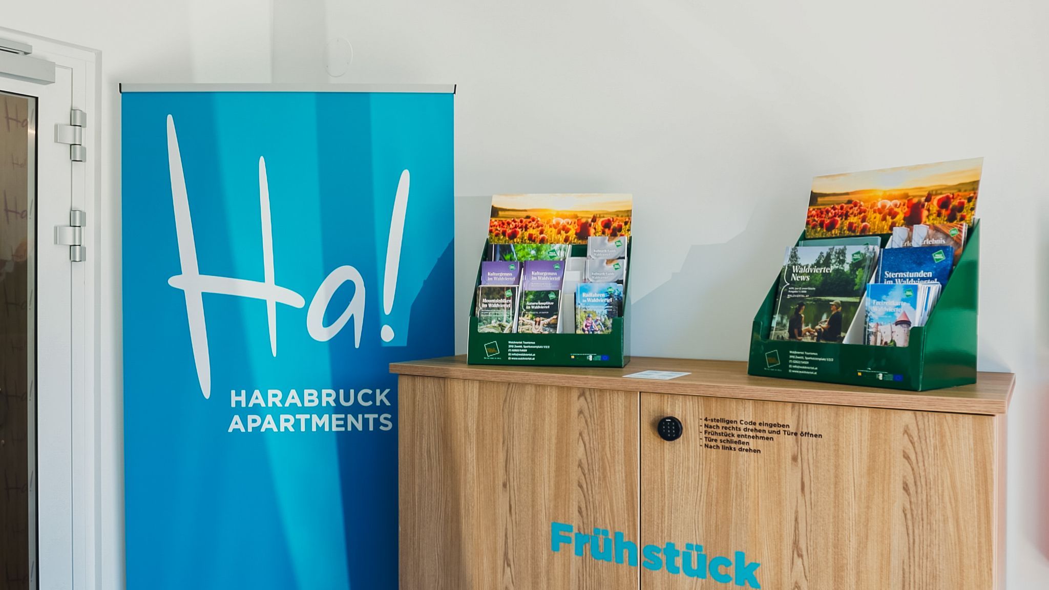 A reception area featuring a blue banner for Harabruck Apartments and a brochure rack on a wooden cabinet.