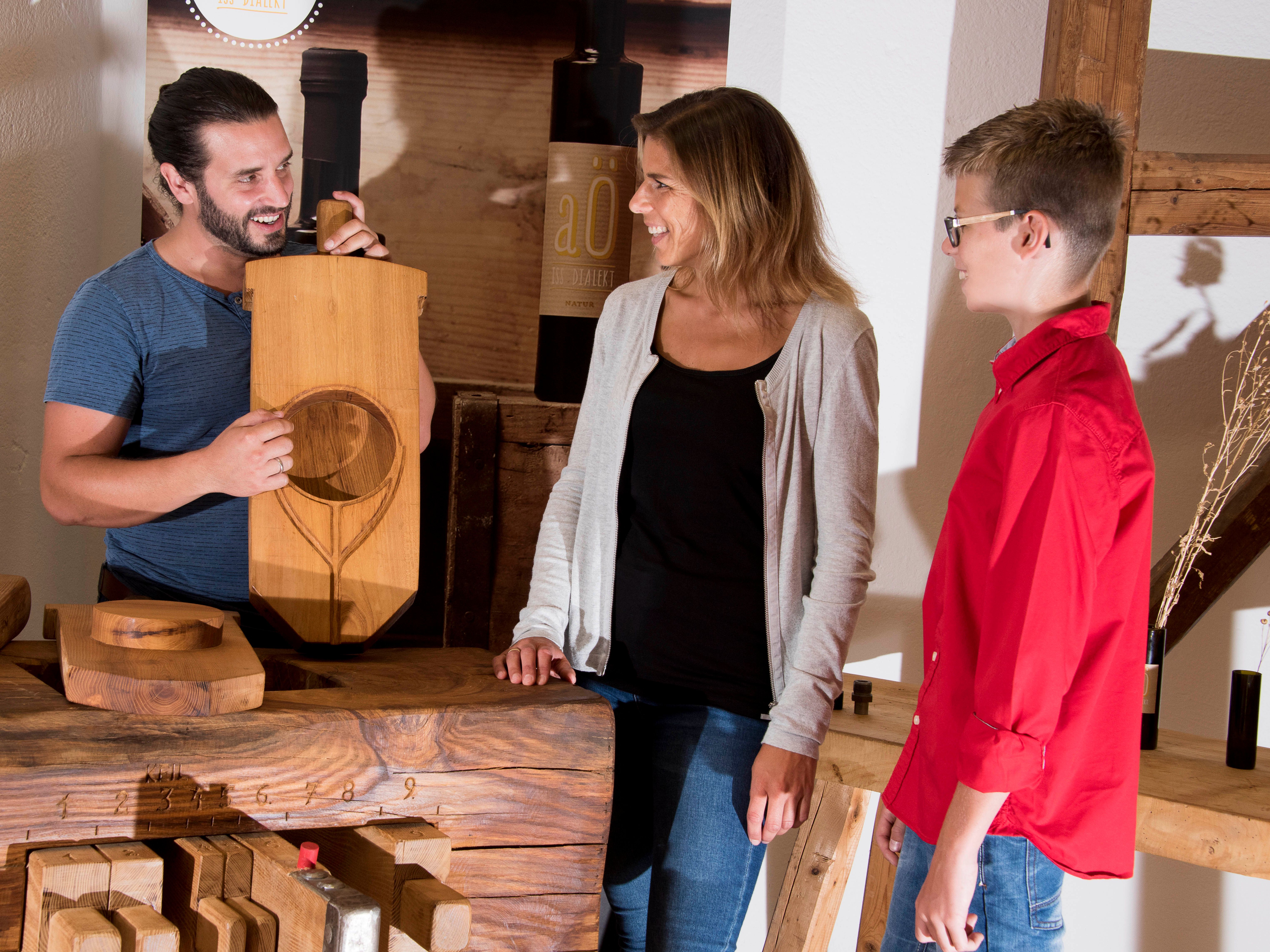 Three people are standing around a wooden table, one person is holding a wooden board with an engraving.