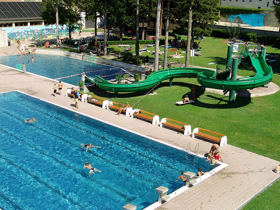 An outdoor pool with two swimming pools, a green water slide and sunbathing lawn.