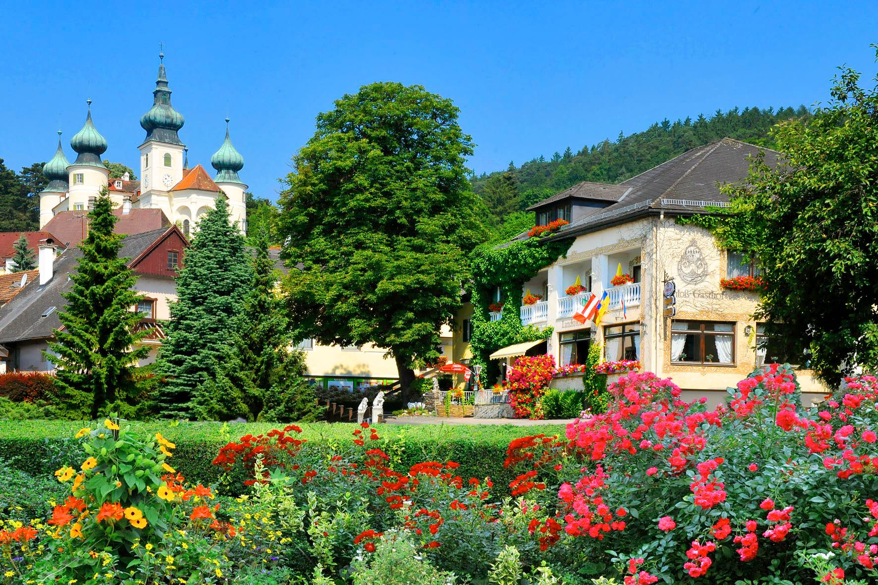A picturesque hotel with colorful flowers in the foreground and a castle in the background.