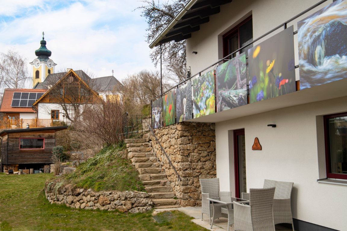A modern house with a balcony and pictures of nature, next to it a church with an onion dome and another building with solar panels.