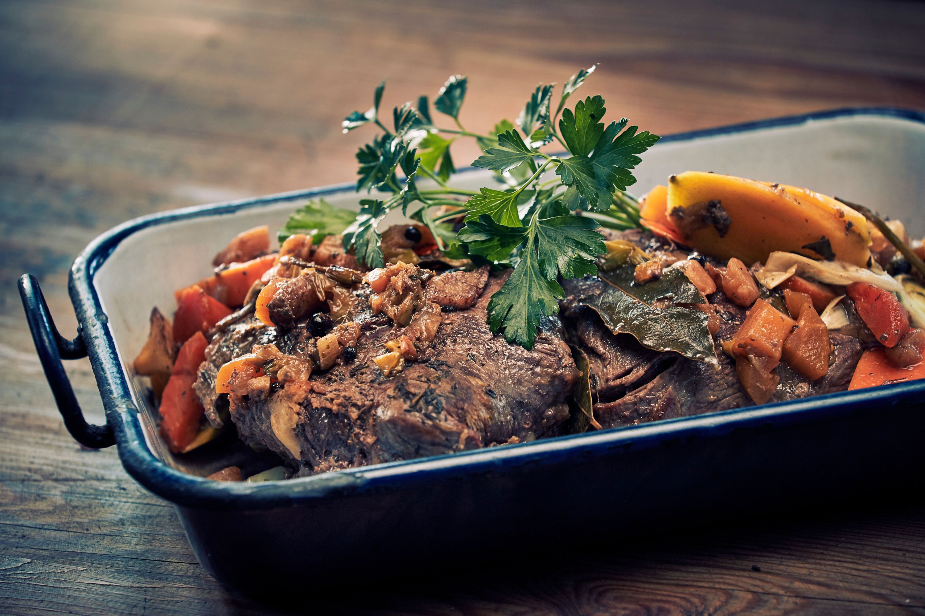 A roast with vegetables and herbs in a casserole dish.