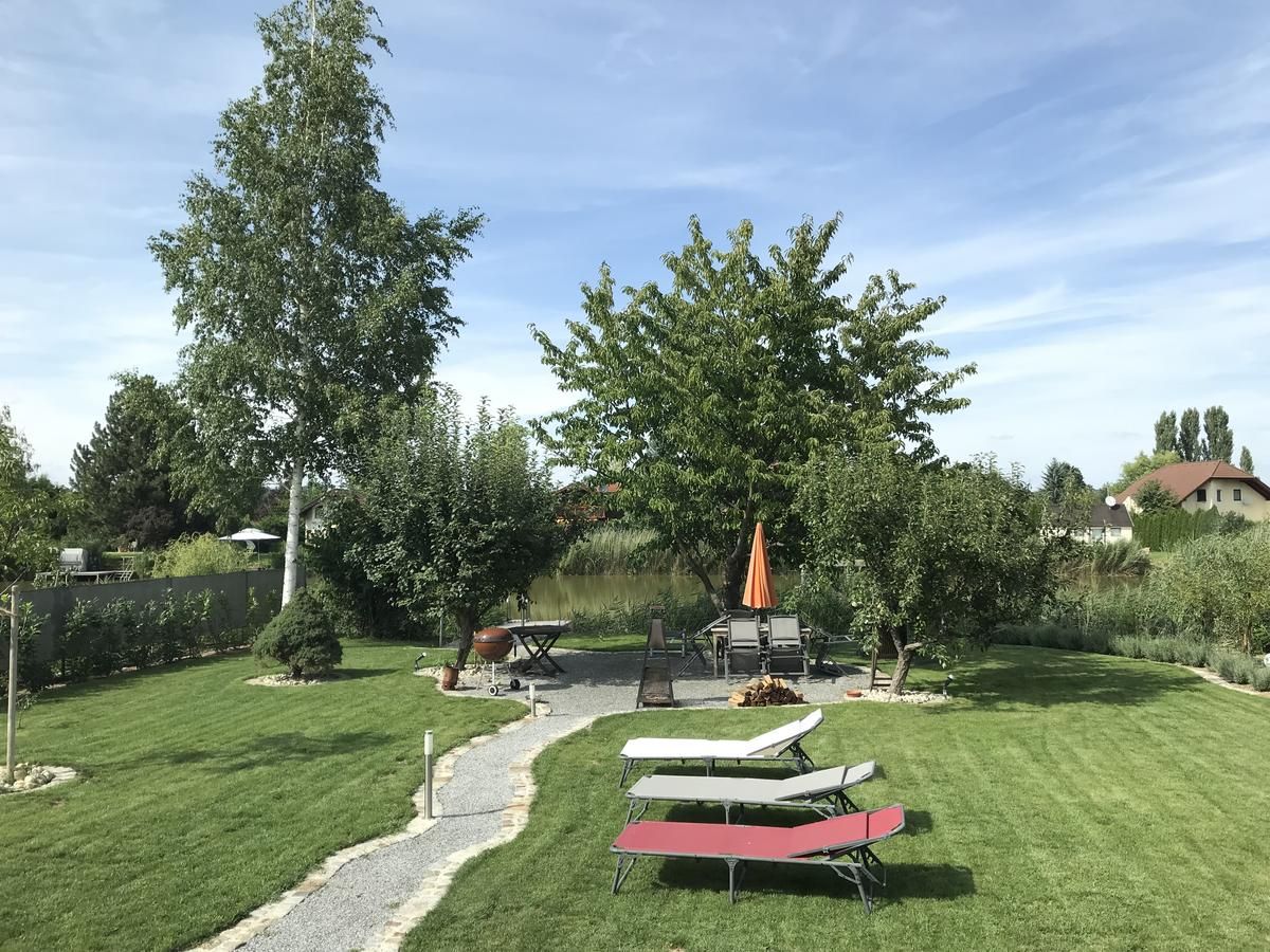 A well-kept garden with lawn, trees, sun loungers and a table with parasol.